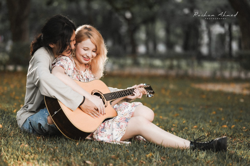 Couple sitting on grass playing guitar