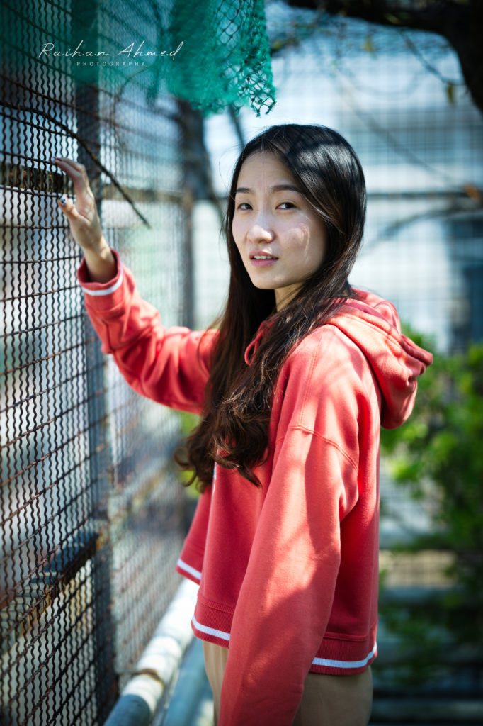 Woman outside against a fence looking into camera